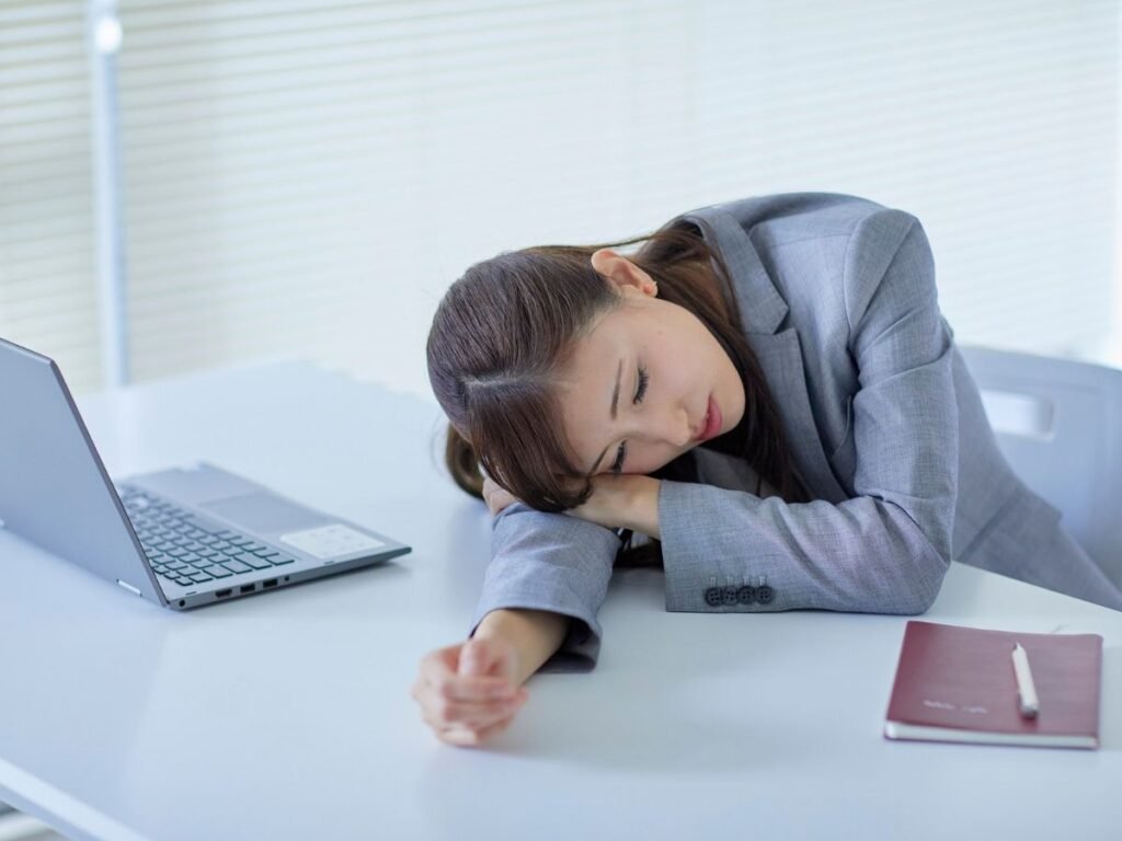 Girl resting head on desk looking exhausted, representing the symptoms of burnout and mental exhaustion.